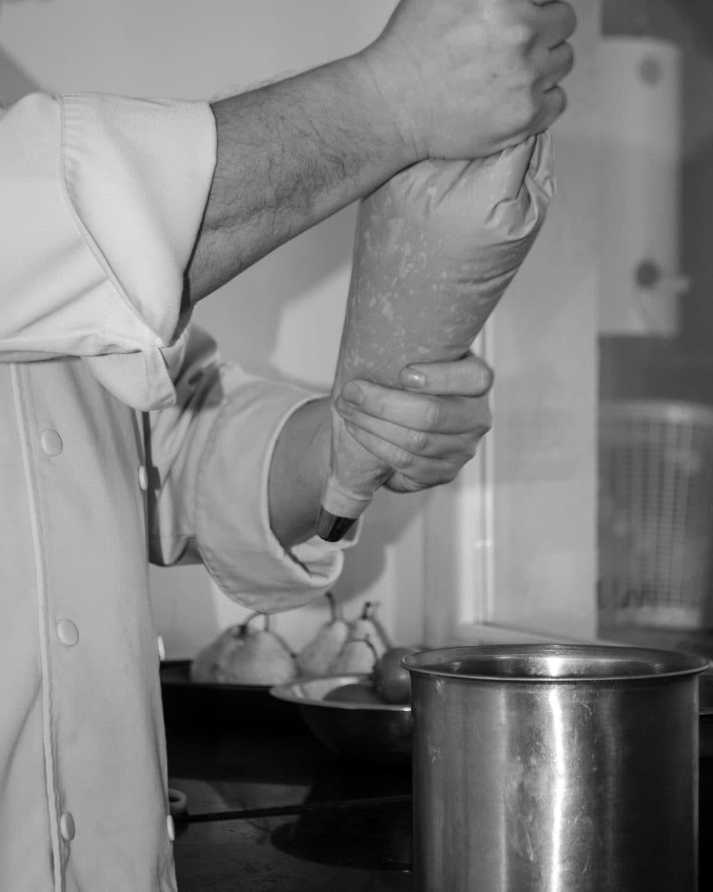 Sus manos apretando una manga pastelera sobre un recipiente de acero