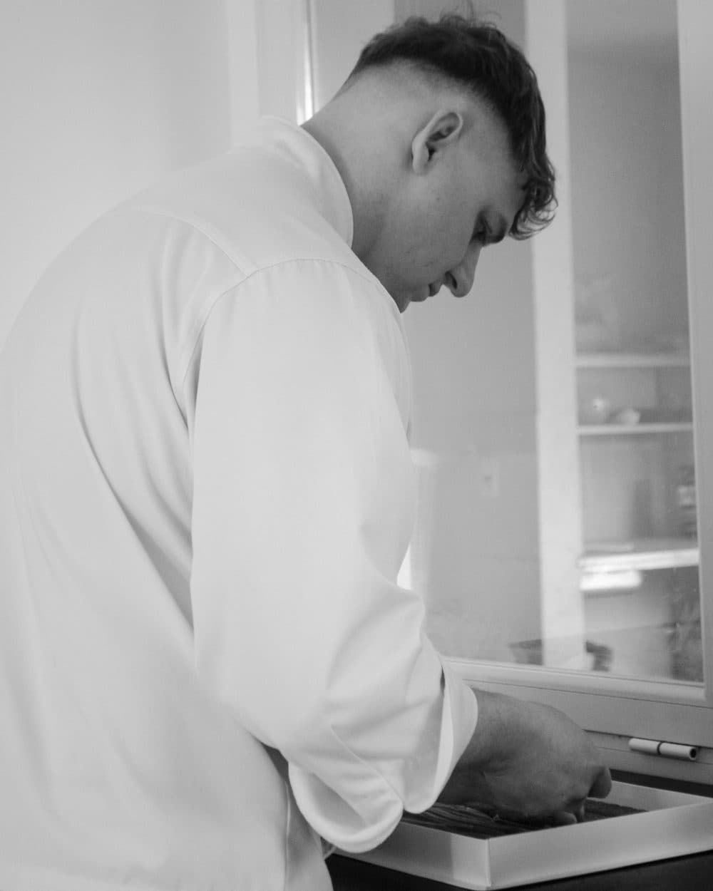 Franco de perfil trabajando sobre una bandeja en la mesada, con la vitrina de la cocina detrás