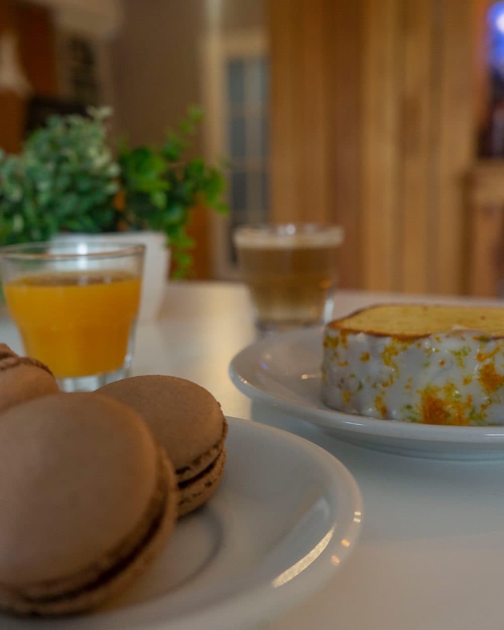 Mesa servida con macarons, jugo de naranja, café con leche y una torta de limón glaseada, en el salón de un hotel