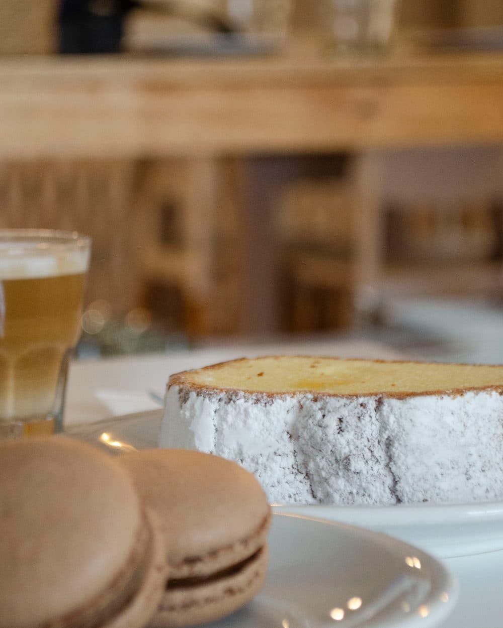 Porción de cheesecake con azúcar impalpable y macarons sobre una mesa, con el salón del hotel desenfocado detrás