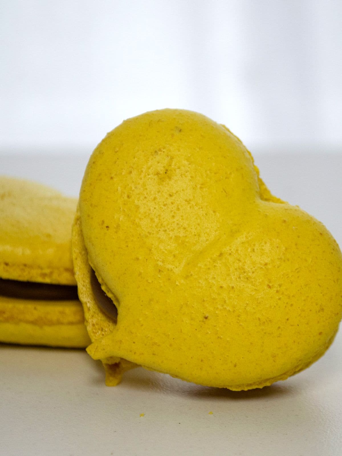 Dos macarons con forma de corazón, amarillos, rellenos de dulce de leche